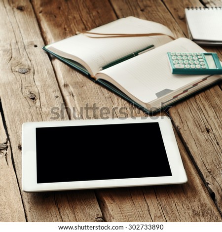 tablet computer with a blank screen on the wooden table with a cup of black coffee, notepads, pencils and calculator. Top view. Copy space. Free space for text.
