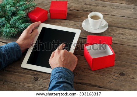 Tablet computer in men hands. Near the table with tablet computer open red gift box, a cup of espresso coffee and fluffy Christmas tree branch Free space for text. top view. Copy space. Closeup