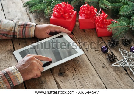Tablet computer in men hands. Near the table with tablet computer three gift boxes, christmas toys, stars , fir cones and fluffy fir branches. Free space for text. top view. Copy space. Closeup