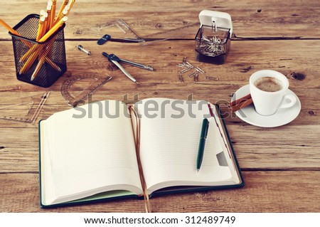 open notebook with blank pages on wooden desk with a cup of coffee and office accessories close up. Copy space