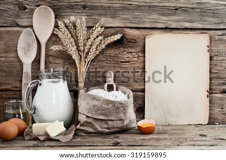 Baking ingredients eggs, flour, milk, butter, sunflower oil on wooden background with a blank sheet. Top view. Free space for text. Food background