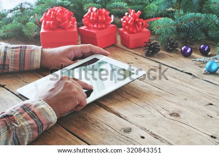 Tablet computer in men hands. Near the table with tablet computer red gift box, christmas toys and fluffy fir branches. Free space for text. top view. Copy space. Closeup