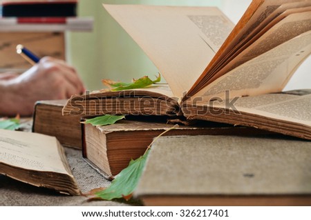 Old books. Old open book close up with autumn leaves on the table. In the background a man hand writing in a notebook. Copy space