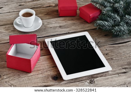 White tablet computer with open Christmas gifts and a cup of coffee on wooden table closeup. Copy space. Free space for text