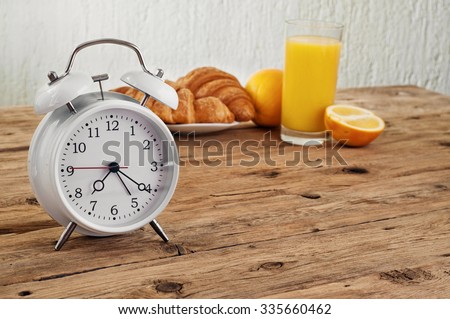 White round alarm clock on a wooden table in the kitchen with croissants and orange juice. Copy space. Free space for text or object