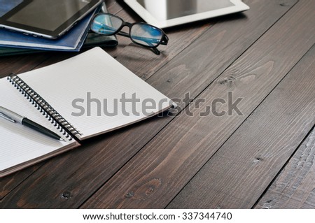 Business Objects (tablet computer, glasses for computer, notebook, leather folders, pen). Open notebook with blank pages on wooden office desk close up. Top view. Free space for text. Copy space