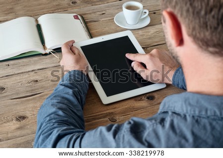 Man working with a tablet computer at a wooden table. The man clicks on the tablet screen closeup. Copy space. Free space for text