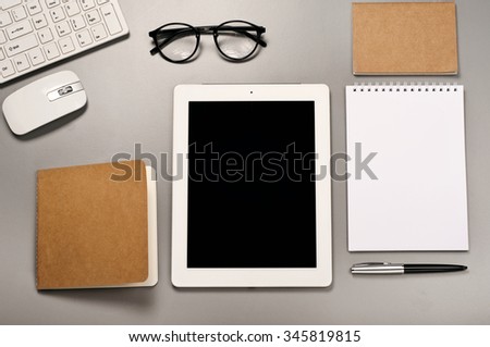 Tablet computer with a keyboard, mouse, glasses, pen and notepad on a grey table. Top view. Copy space. Free space for text. Office desk mock up