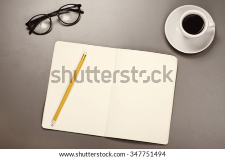 Open notebook with blank pages with a pencil, glasses and coffee cup on a grey surface. Top view. Business background