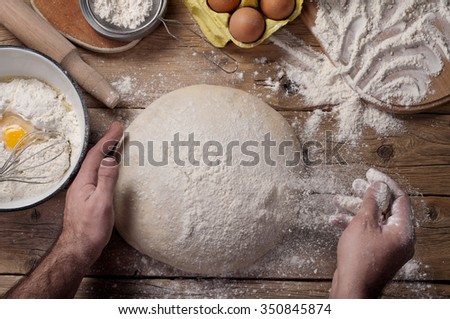 Male baker prepares bread. Male baker sprinkle the dough with flour. Making bread. Top view. Rustic style