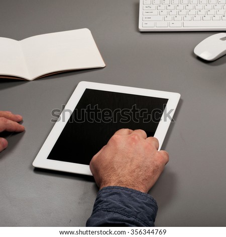 Man working with a tablet computer. Man clicks on the screen tablet computer on a gray office table. Top view. Square frame