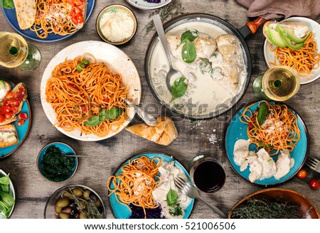 Traditional Italian food table, classic pasta with tomato sauce, chicken breast in a creamy sauce with mushrooms, snacks and red and white wine, top view