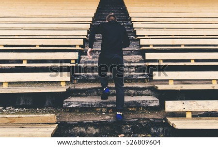 Young man runner in sport clothes running climbing stairs in the stadium