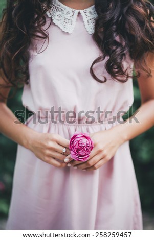 Young woman in a pink dress holding little pink rose in her hands. Close-up