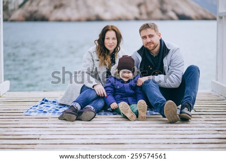 Happy family -mother, father and little son- walking in harbor near sea. Family wearing fashion clothes