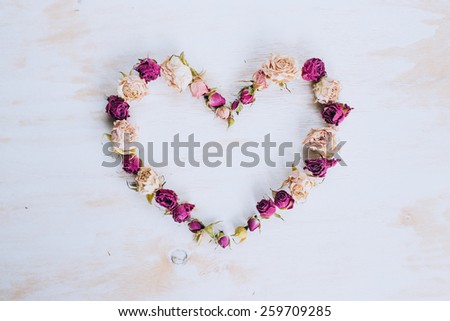 Dry rose flowers in heart shape on old wooden background. Shabby-chic