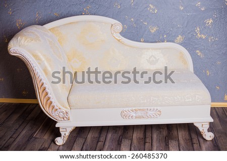 White and gold Baroque couch standing near textured wall on a wooden floor. Classic interior