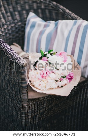 Peonies packed in craft paper lying on a wicker chair near pillow