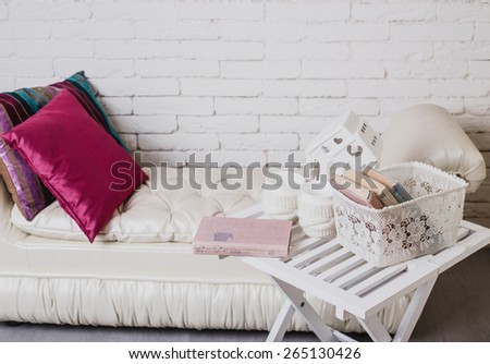 Interior details. White brick wall. Part of interior with couch and decorative pillows, white wooden table with books on it