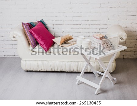 Interior details. White brick wall. Part of interior with couch and decorative pillows, white wooden table with books on it