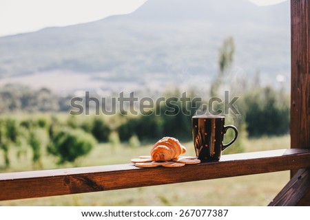 Cup of hot tea and croissant on balcony with mountains behind