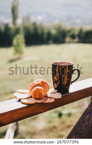 Cup of hot tea and croissant on balcony with mountains behind