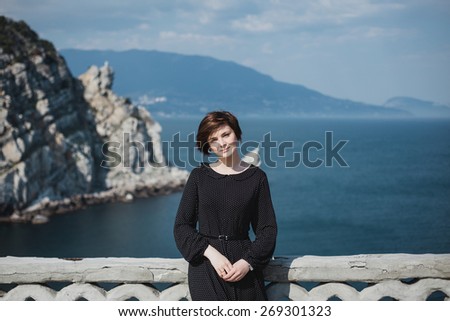 Young pretty woman with a short haircut standing on a balcony in a fashion dress with beautiful view on the background