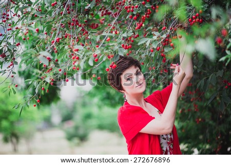 Young woman with short haircut standing near cherry tree with red cherries