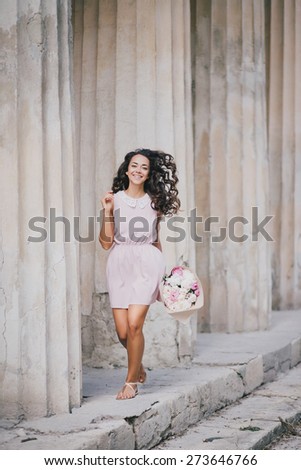 Beautiful girl in a pink dress with a bouquet of peonies posing near old columns. Spring mood