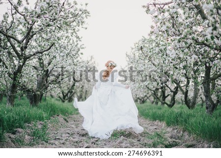 Beautiful bride in a vintage wedding dress running in a blooming apple garden. Spring mood. Young woman in a white vintage dress