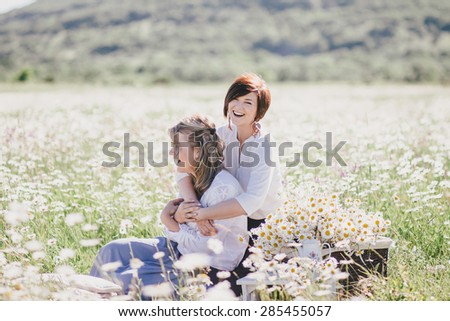 Two young pretty women having picnic with tea in chamomile field. Female friendship