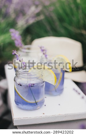 Homemade lavender lemonade with fresh lemons on a white wooden tray in a lavender field