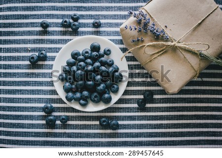Plate with blueberries and a present wrapped in a craft paper standing on a striped tablecloth