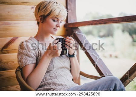 Woman sitting in a wicker chair on a cozy balcony with a cup of tea