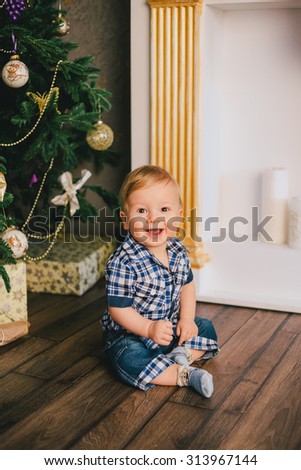 Smiling baby-boy sitting under Christmas tree near fireplace