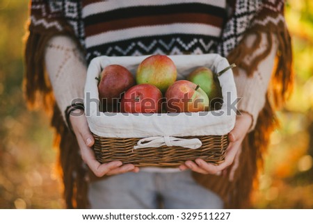 Young woman wearing knitted poncho having picnic in a forest: drinking tea and picking apples. Fall concept