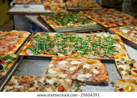 Multiple types of pizza in pans in pizzeria.