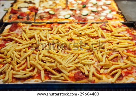 Pizza with french fries on pan in pizzeria.