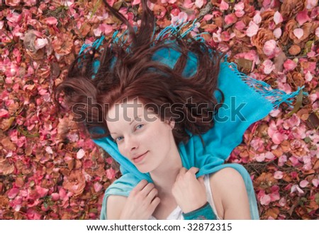 Young woman laying on ground on blue scarf on ground covered with pink petals. Shallow depth of field.