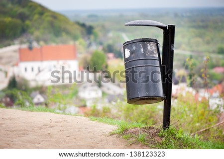 Single black metal empty rubbish bin on the hill and blurred dale view in Kazimierz Dolny, Poland, lubelskie. Object stick in tourist place with view at all town valley landscape, horizontal, nobody.