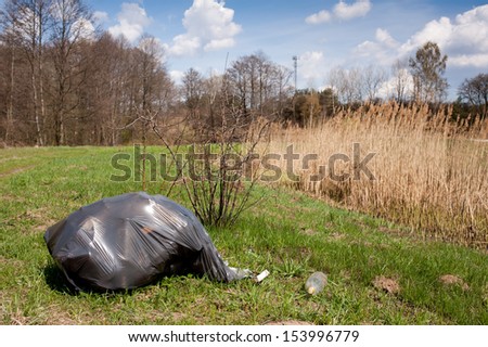 Illegal scatter garbage in black plastic bag dump in woods lying on fresh grass in early spring season, Clean Up the World gathering in Poland. Earth Day and nature dispose, horizontal orientation.