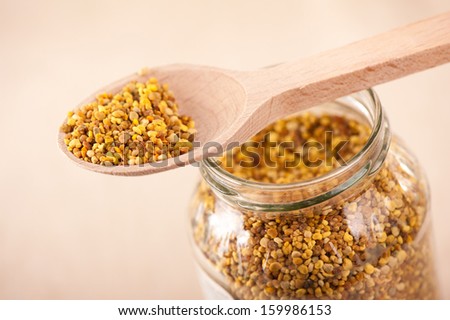 Fresh yellow pollen grains portion in wooden spoon and glass jar, plants seeds are healthy food ingredient. Horizontal orientation, studio shot.