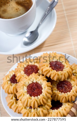 Many cookies with jelly and black coffee in cup, little teaspoon lying on saucer. Aromatic traditional beverage with delicious and decorated cookies with red jelly, vertical orientation