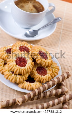 Jelly cookies pile and black coffee in cup, little teaspoon lying on saucer. Aromatic traditional beverage with delicious and decorated cookies with red jelly, vertical orientation