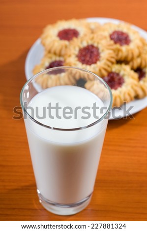 Milk glass and jelly cookies on table, healthy beverage with delicious and decorated cookies with red jelly, vertical orientation, objects lying on table, studio shot, nobody.