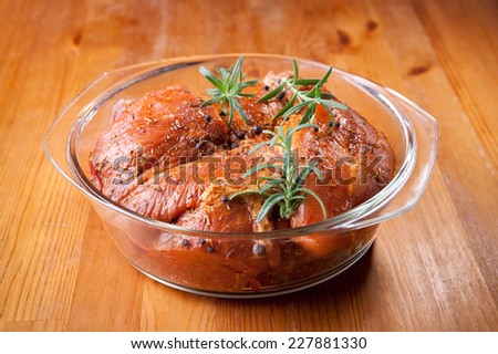 Raw pork meat flavored with rosemary twigs in glass dish on table in horizontal orientation, nobody.