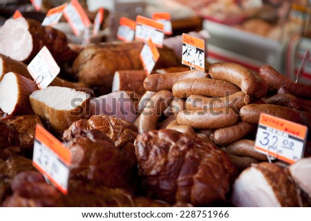 Smoked sausages and ham in bazaar stand. Shop display with meat products, many alternatives to choose, with prices stick in, horizontal orientation, nobody, real photo.