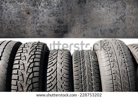 Group of used black tires in row and black metal sheet background, old objects detail in open air, horizontal orientation, nobody in frame.