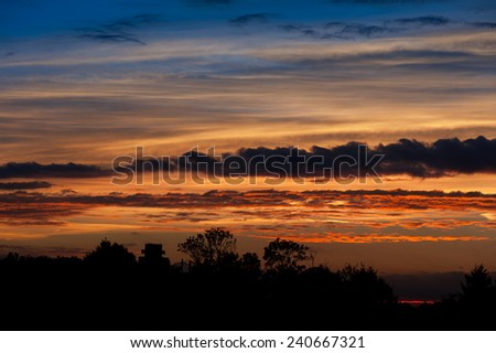 Twilight colorful sunset with trees silhouette in Warsaw, Poland, Europe. Awesome dark warm sunlight and beautiful clouds formation, cloudscape and sunny weather in horizontal orientation, nobody.