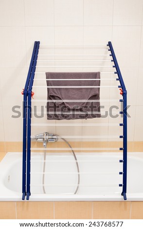 Foldable over bath folding blue clothes horse drying rack, indoor airer tool white color on bathtub, nobody, vertical orientation.